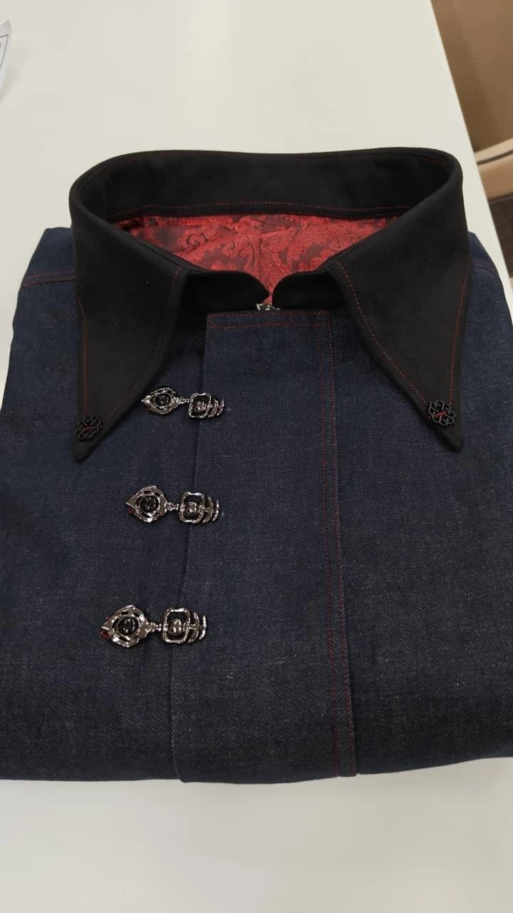 A carefully folded dark denim shirt with a black collar, red lining, and three sculpted silver clasps.