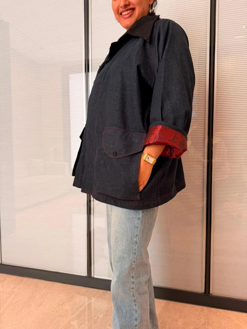 A dark denim jacket worn with pale jeans, its turned-back cuff revealing a red patterned lining.