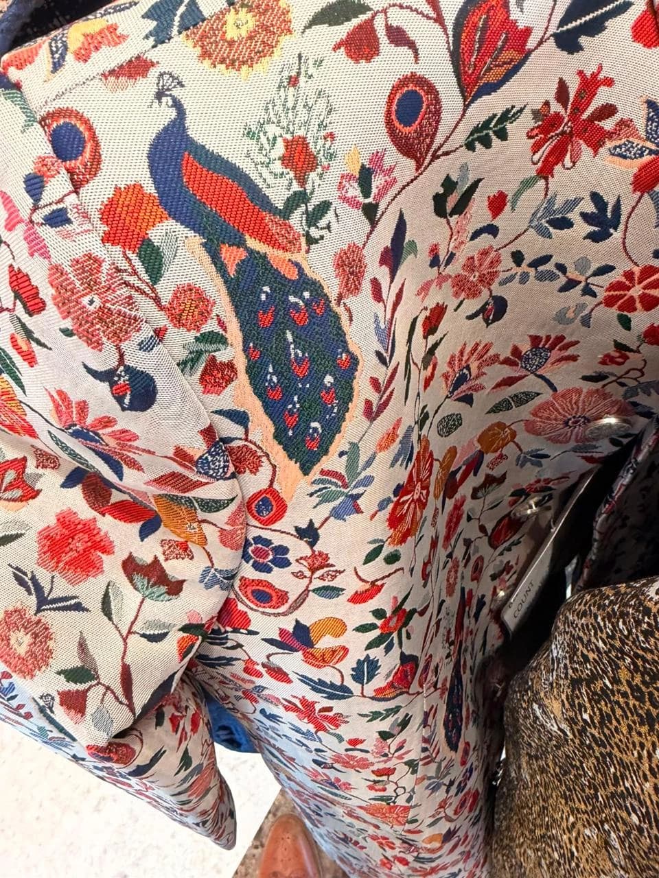 A close view of a richly woven fabric with blue peacocks, red flowers, and winding green stems.